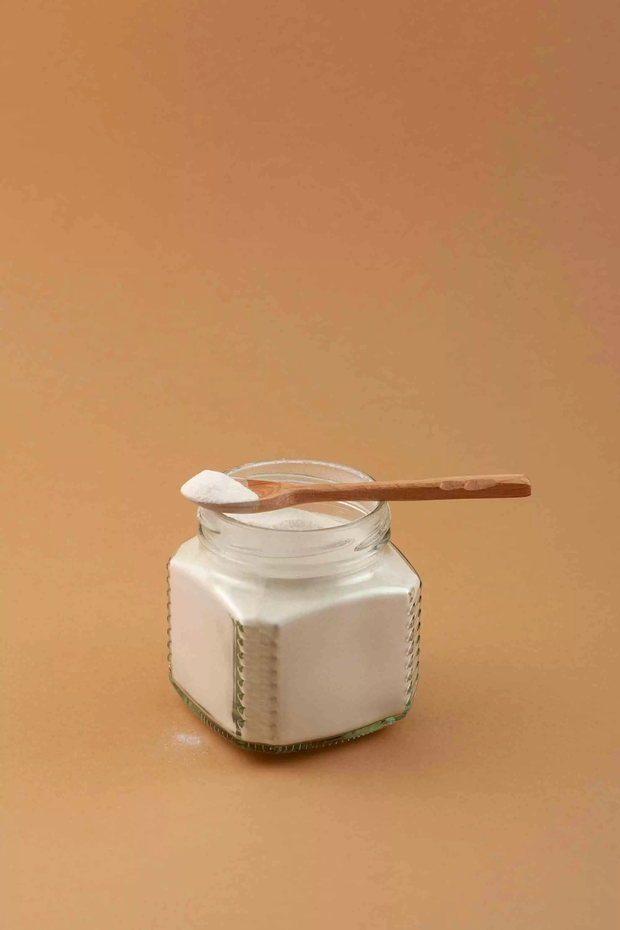 powder A jar of white powder with a wooden spoon on a orange background.